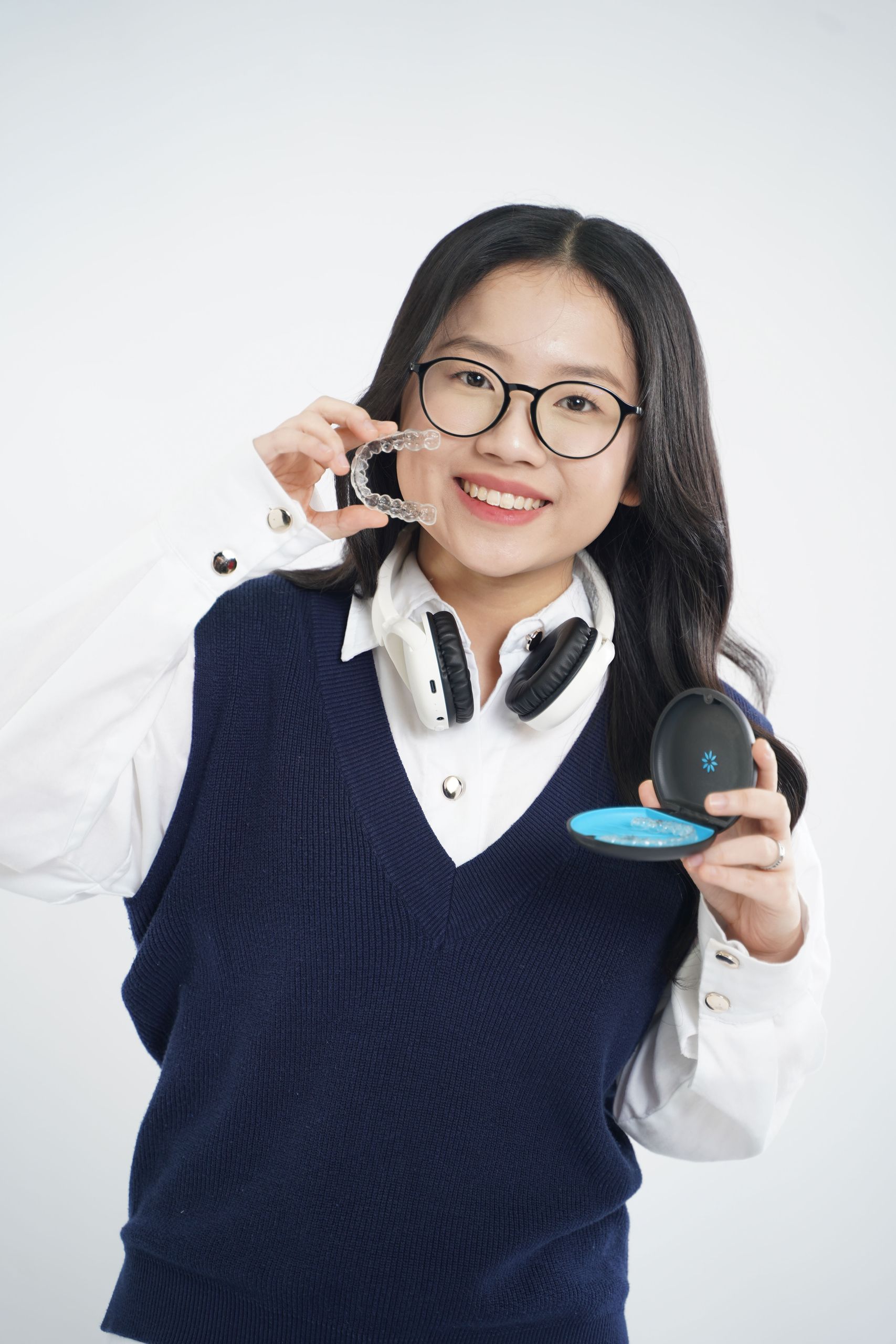 Happy woman displaying clear aligners with headphones around neck