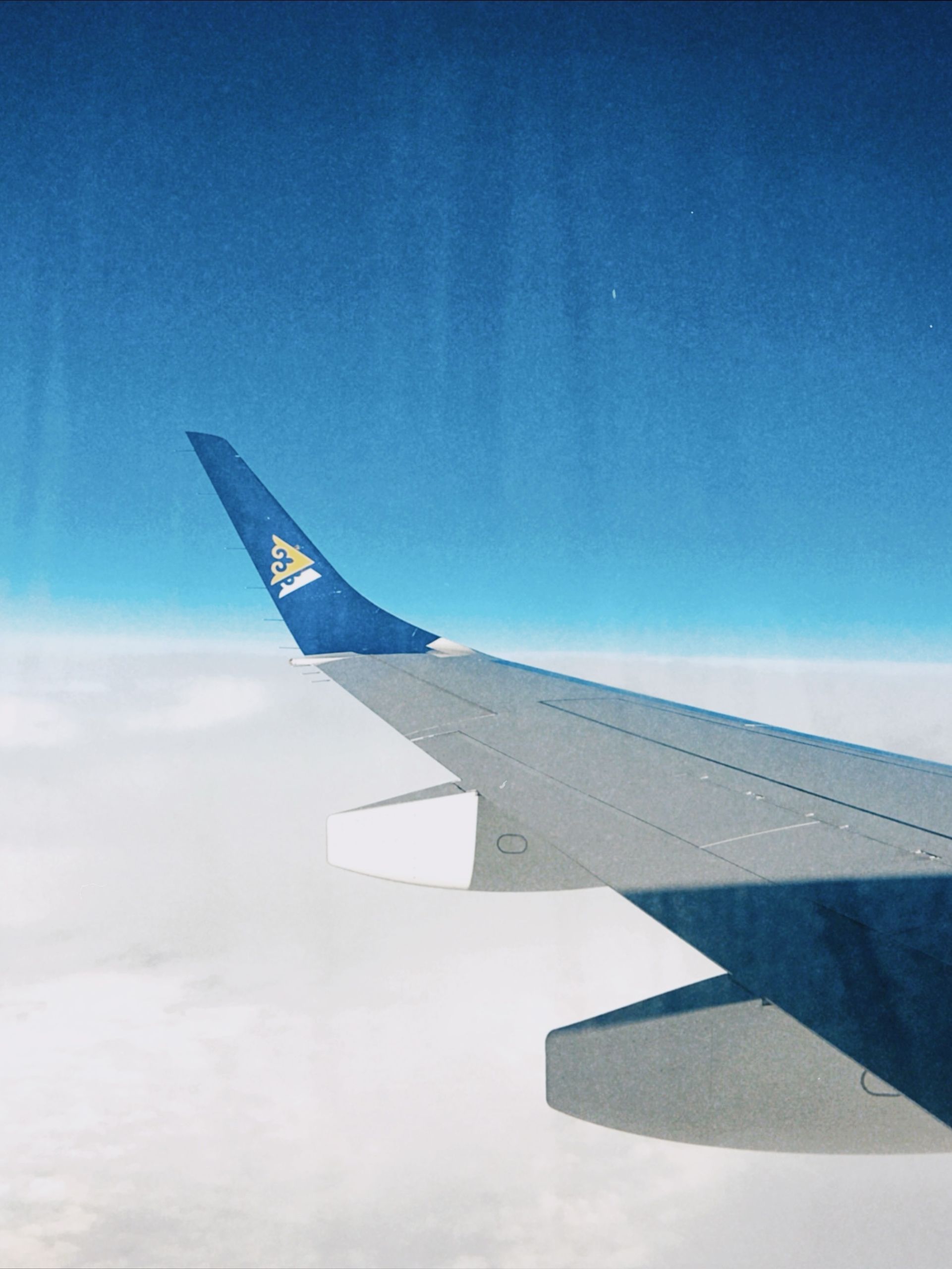 Wing of an airplane flying high over Kazakhstan with clear blue skies and clouds.